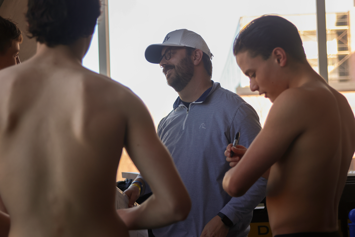 Junior Turner Bruce writes his events in sharpie on his arm while Head Coach Brian Kirkpatrick gives a peptalk