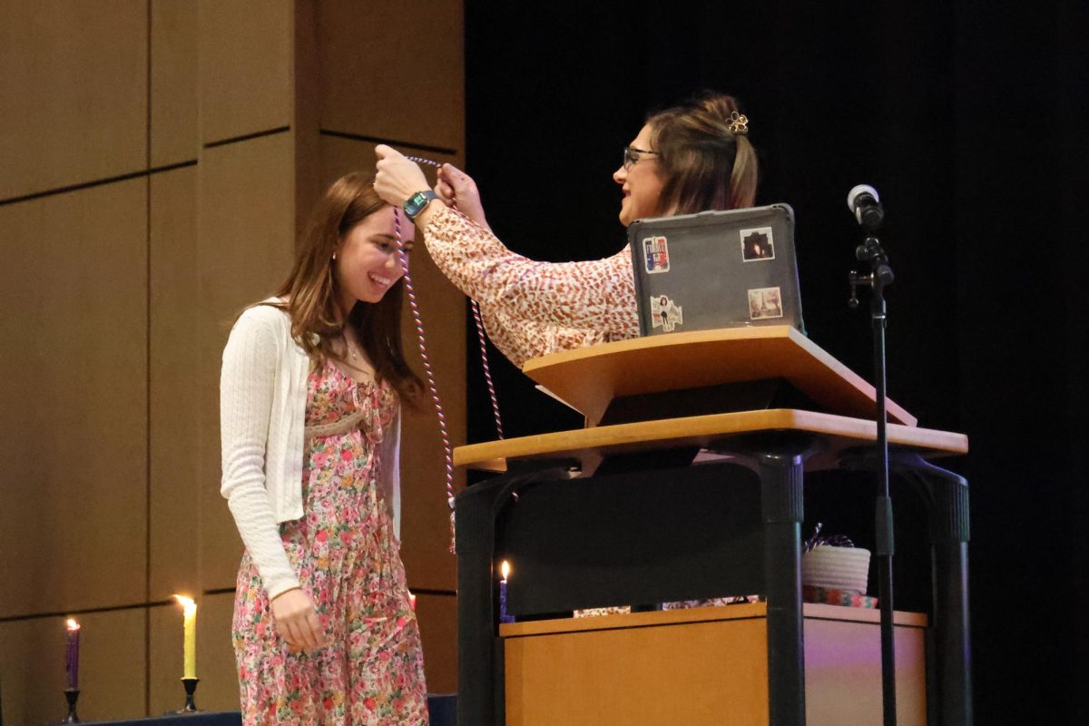 Madame Smith honors senior member Gwen Kline with a graduation cord during the French NHS induction ceremony.