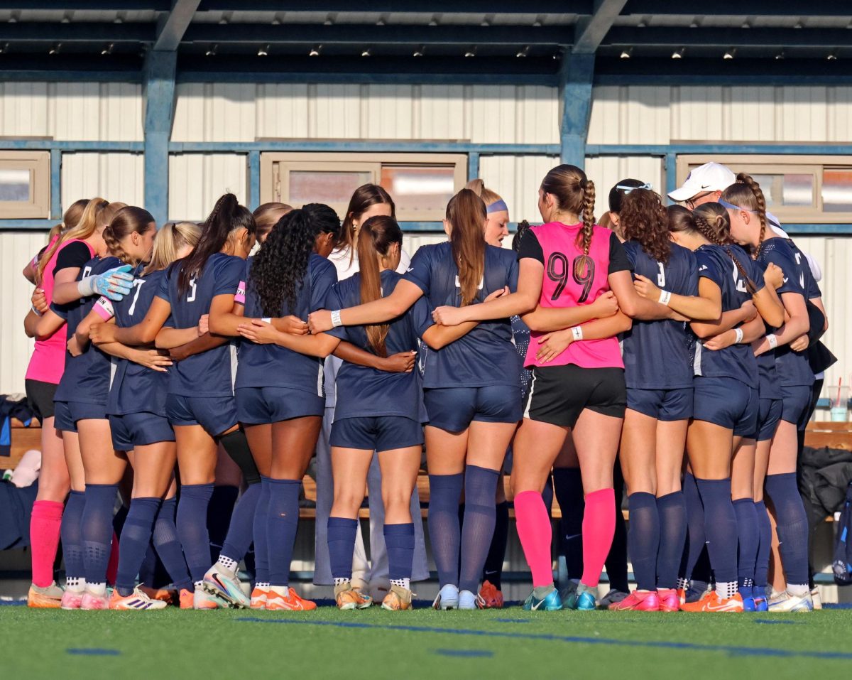 Each player wraps their arms around the others for the pregame huddle.