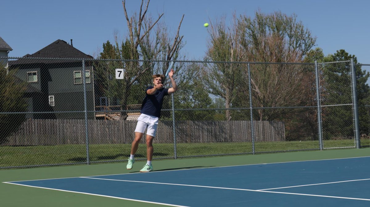 Arm outstretched, junior Gage Horn swings at the ball to complete his serve.