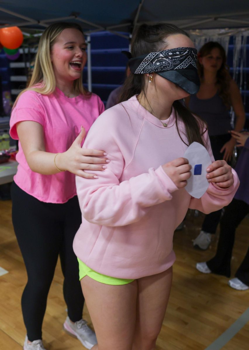 Laughing, senior Piper Ross guides senior Bianca Pepe to pin a football on a cardboard cutout of Travis Kelce