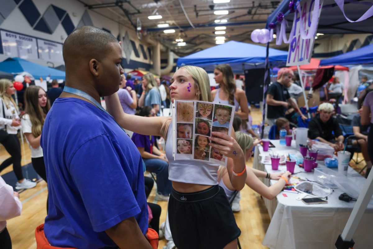 Focused, junior Ella Ericson does a face paint design on junior Quyncee Graves.