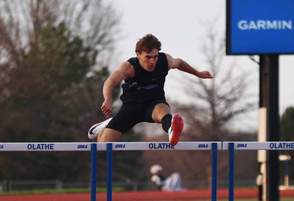 Arms out, junior Charles Bullard runs over the hurdle.