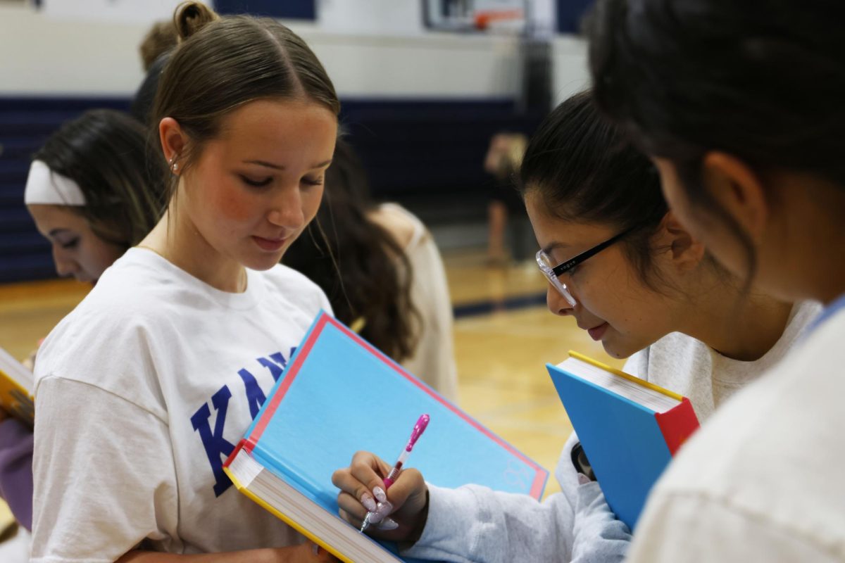 Leaning in, junior Isabella Simon signs junior Cadence Buum's yearbook to preserve memories with her classmate, Friday, May 15.