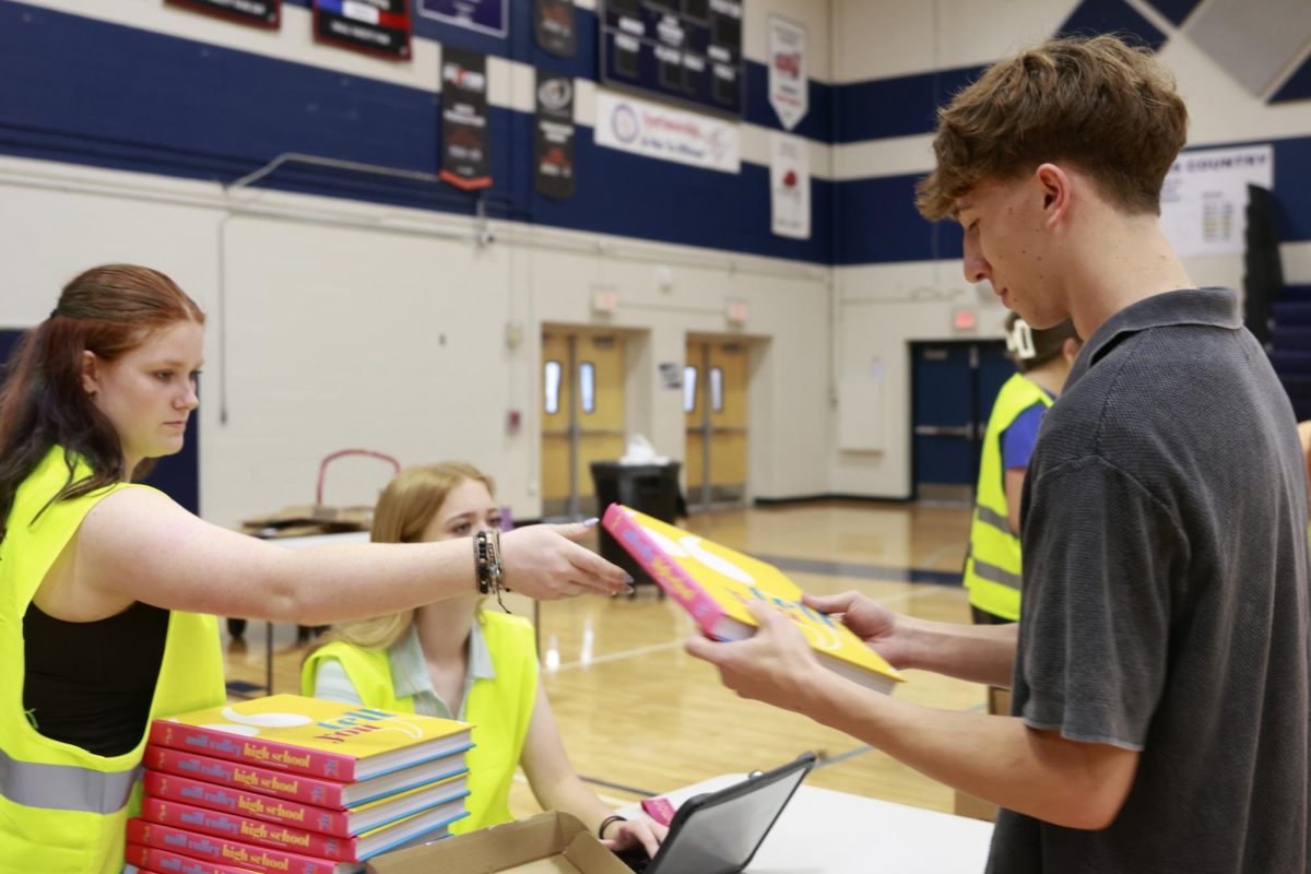 Junior Charlie Barret hands sophomore Noah Lauer his yearbook.