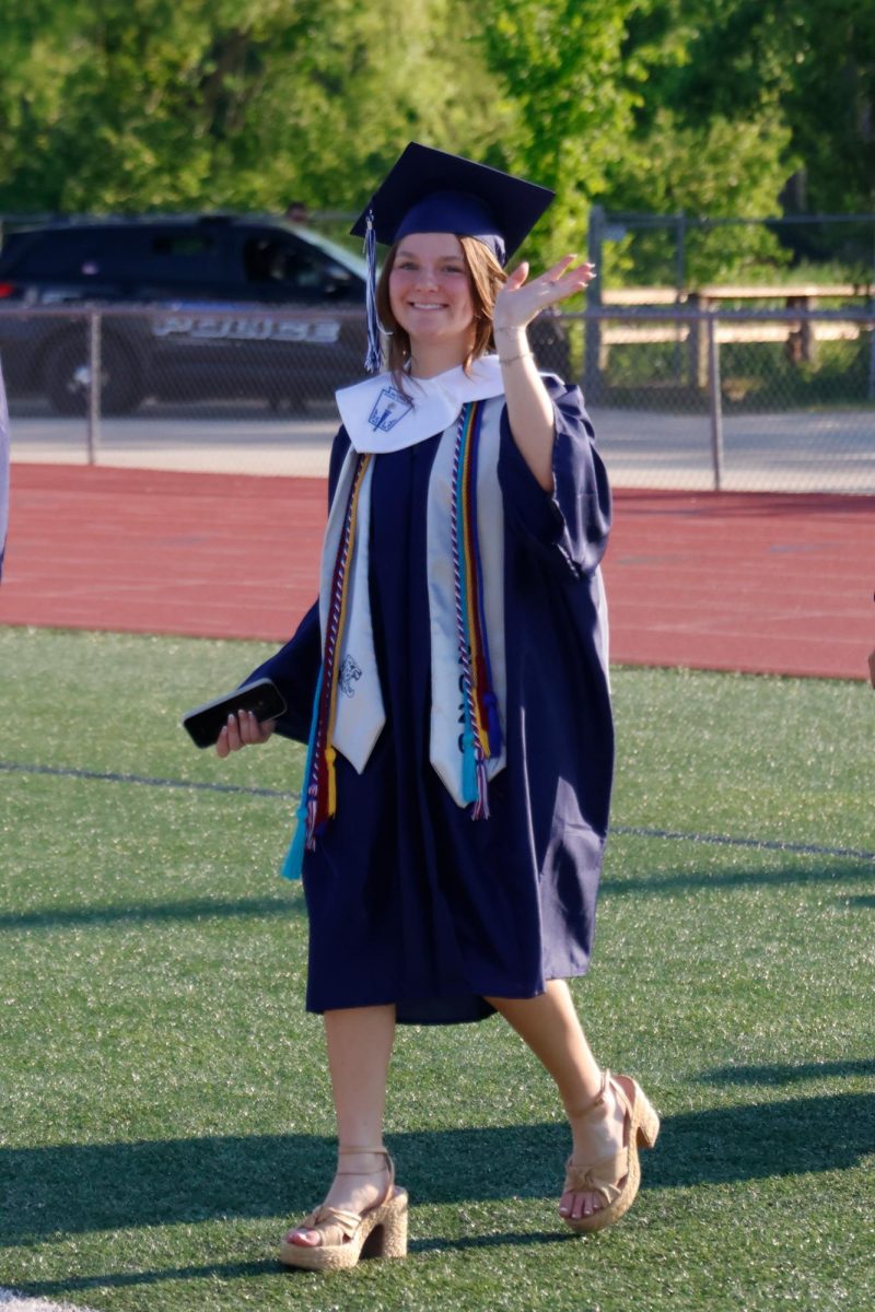 Waving to the camera, senior Maddie Martin walks to her seat.