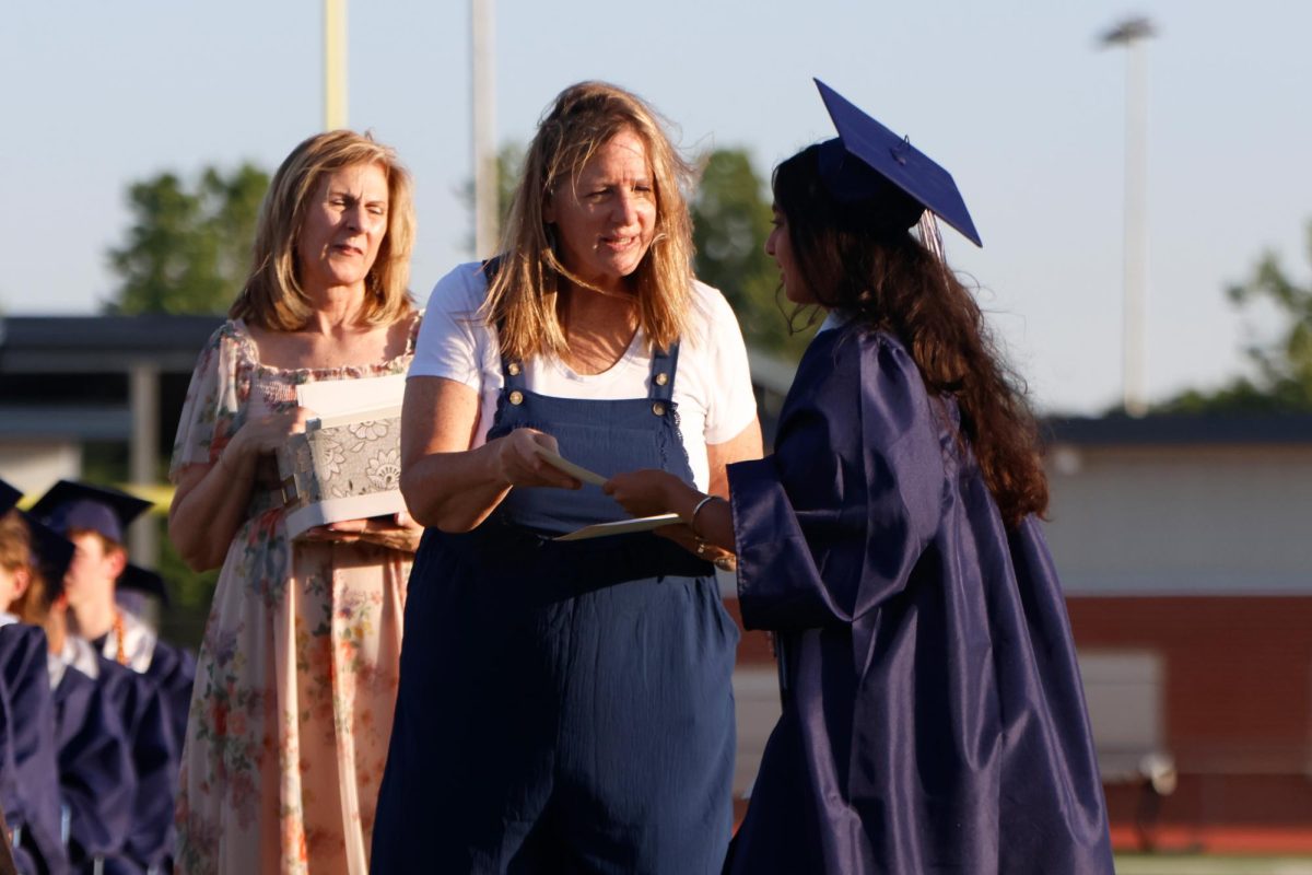 Handing a card to a graduate, registrar Deana Thom directs seniors to their seats.
