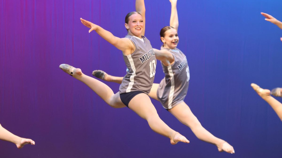 Junior Chloe Thomas smiles towards the audience while performing their dance and leaping in the air