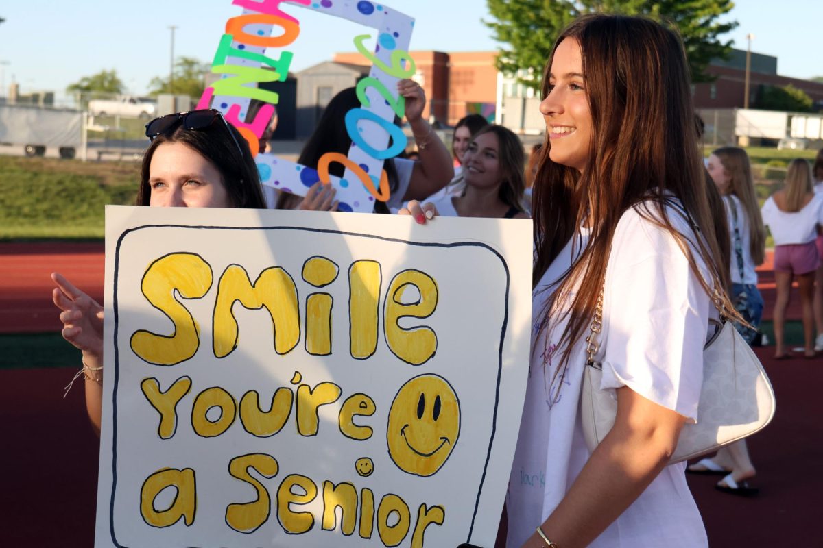 Smiling, seniors Callie Smouse and Lilly Feuerborn pose with a senior sign.