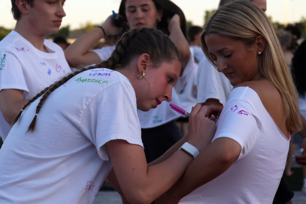 Focused, senior Sydney Nash signs her name on senior Mallory Lux's shirt