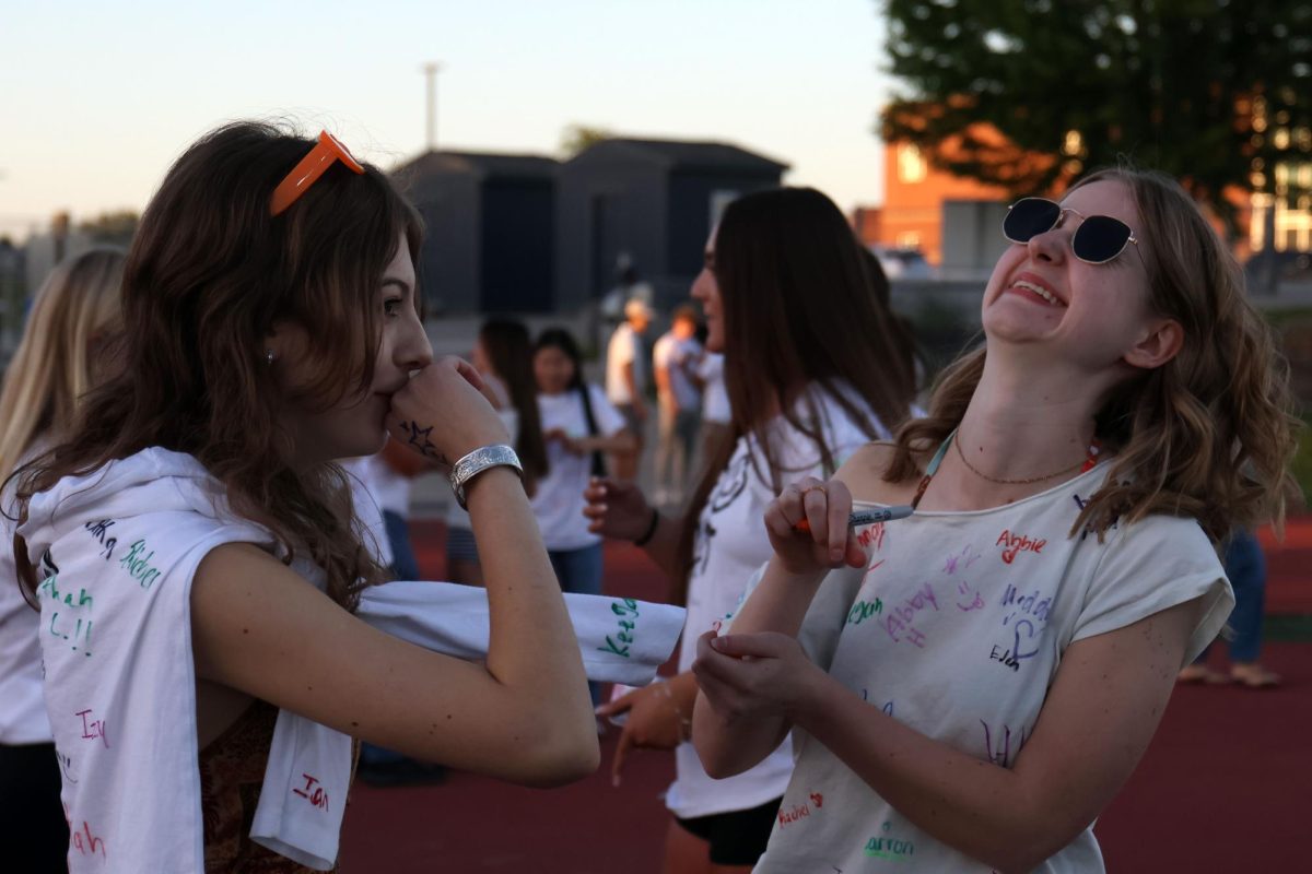 Pen in hand, senior Jordan Powell laughs with senior Mia Plumberg as they sign one another's shirts.